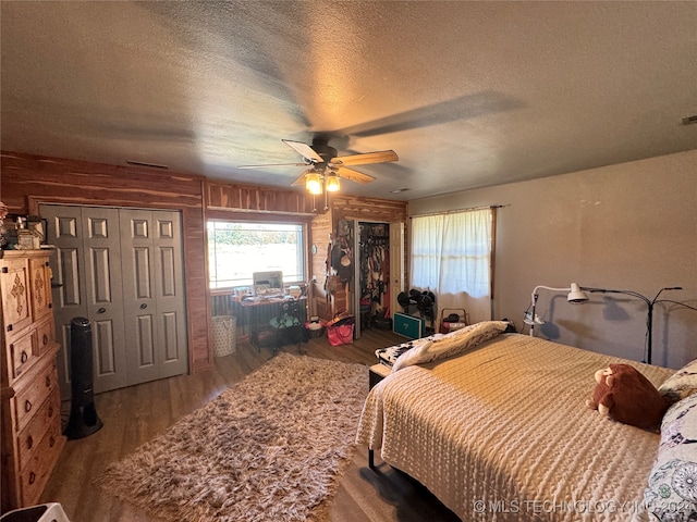 bedroom with wood walls, ceiling fan, hardwood / wood-style floors, a closet, and a textured ceiling