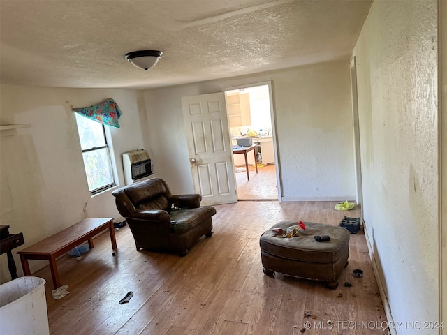 living area with heating unit, light hardwood / wood-style floors, and a textured ceiling