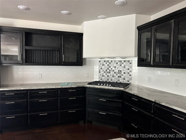 kitchen with stainless steel gas stovetop, light stone countertops, dark wood-type flooring, and backsplash