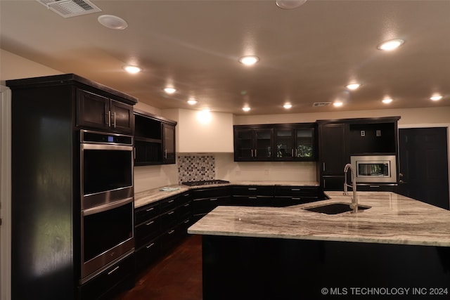 kitchen featuring a center island with sink, sink, light stone countertops, and stainless steel appliances