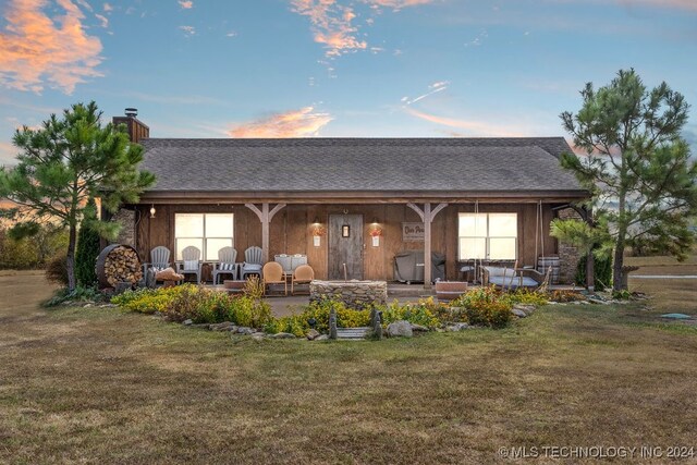 back house at dusk featuring a lawn and a patio area