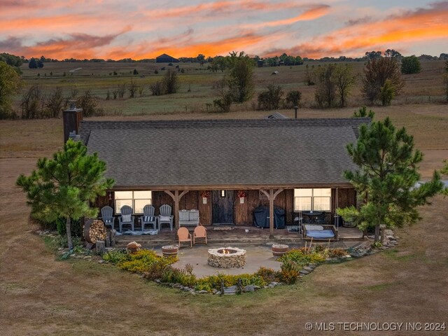 back house at dusk with an outdoor fire pit, a patio area, and a rural view