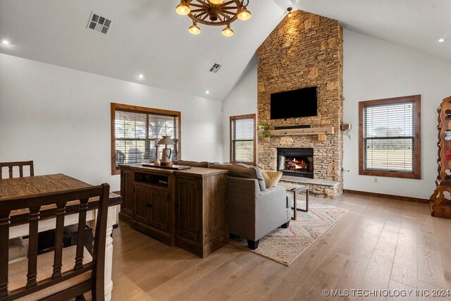 living room with a stone fireplace, light hardwood / wood-style floors, high vaulted ceiling, and a healthy amount of sunlight