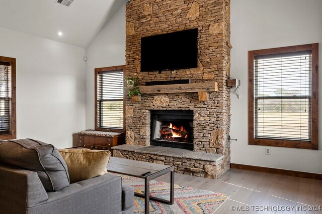 living room with high vaulted ceiling, a stone fireplace, and light hardwood / wood-style flooring