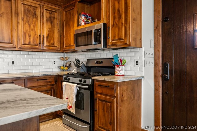 kitchen featuring appliances with stainless steel finishes, light stone counters, and decorative backsplash