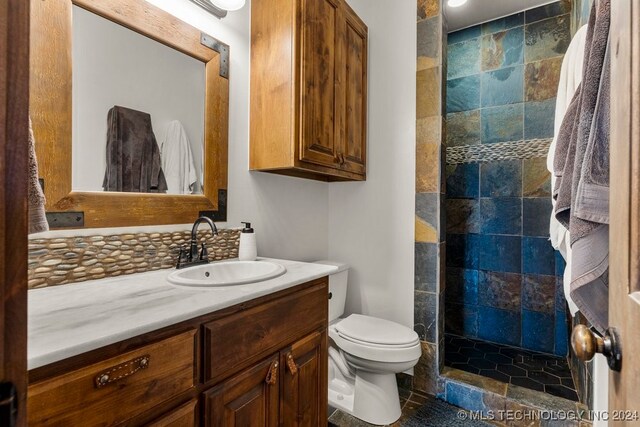 bathroom featuring a tile shower, vanity, and toilet