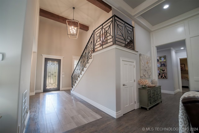 foyer featuring dark wood-type flooring, a towering ceiling, an inviting chandelier, ornamental molding, and beam ceiling