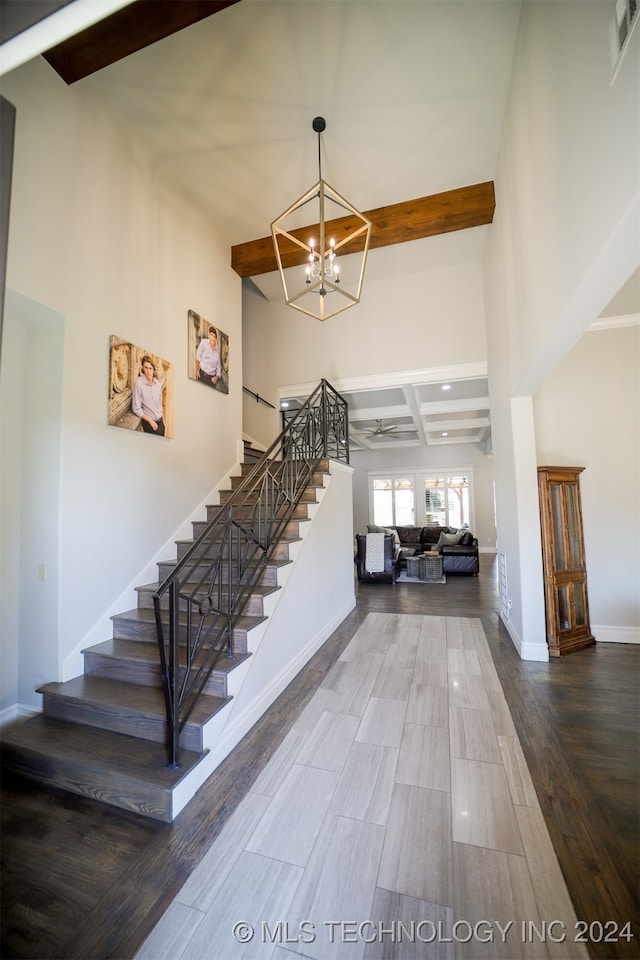 stairway featuring ceiling fan with notable chandelier, a high ceiling, hardwood / wood-style floors, and beam ceiling