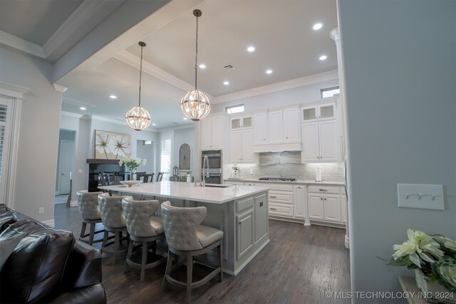 kitchen with decorative light fixtures, a center island with sink, white cabinetry, dark hardwood / wood-style flooring, and decorative backsplash