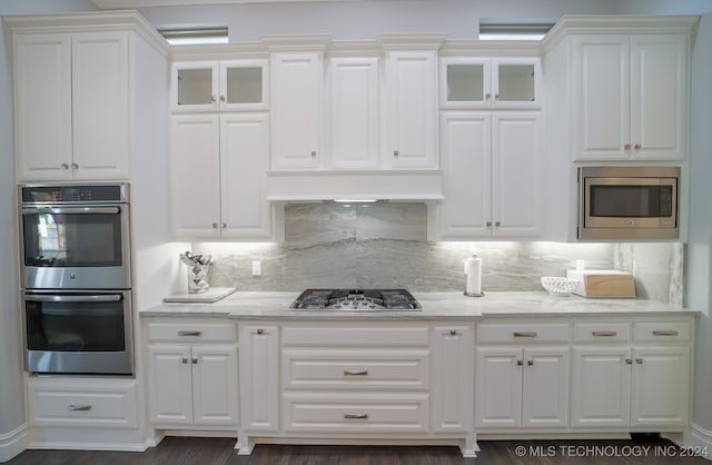 kitchen featuring stainless steel appliances, backsplash, light stone counters, and white cabinetry