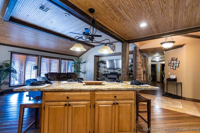 kitchen with a chandelier, decorative light fixtures, light stone counters, a kitchen bar, and a center island