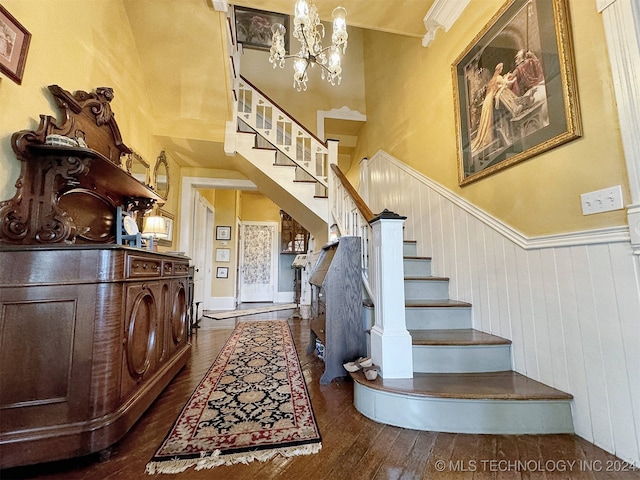 stairway featuring wood-type flooring, an inviting chandelier, a towering ceiling, and ornamental molding