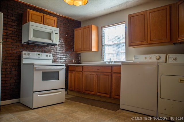 kitchen with white appliances, brick wall, a textured ceiling, and washer and clothes dryer