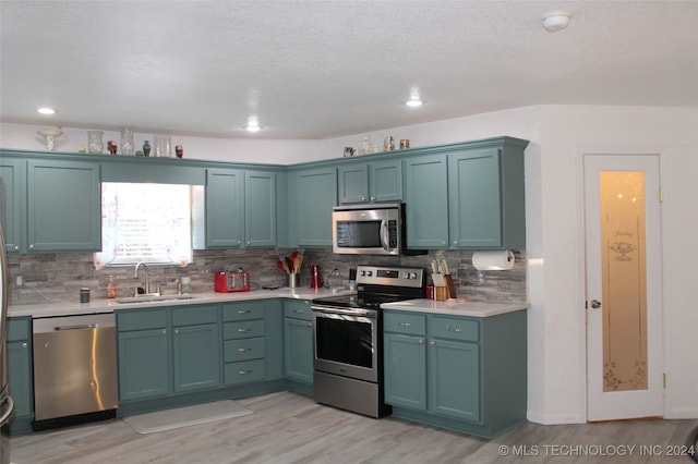 kitchen with backsplash, stainless steel appliances, light wood-type flooring, and sink