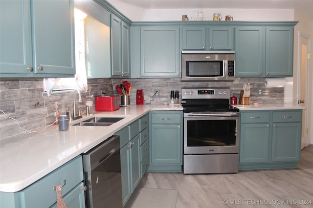 kitchen with light hardwood / wood-style floors, blue cabinetry, sink, stainless steel appliances, and backsplash