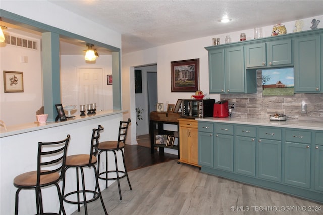 kitchen featuring backsplash, a breakfast bar area, light wood-type flooring, and a textured ceiling