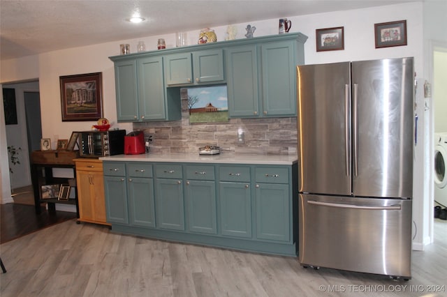 kitchen featuring backsplash, stainless steel refrigerator, washer / clothes dryer, and light hardwood / wood-style flooring