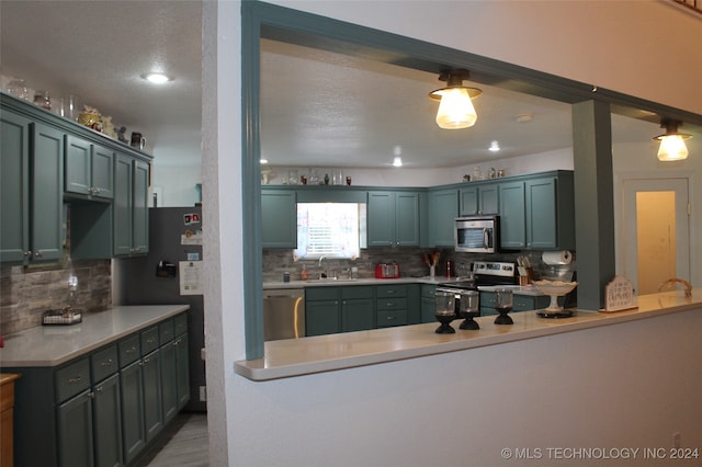 kitchen featuring pendant lighting, tasteful backsplash, sink, stainless steel appliances, and kitchen peninsula