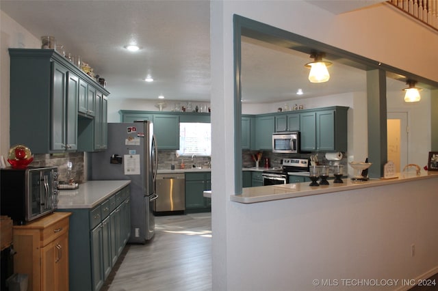 kitchen with stainless steel appliances, light hardwood / wood-style floors, kitchen peninsula, pendant lighting, and backsplash