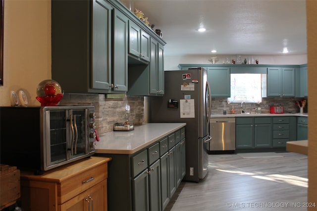 kitchen with backsplash, stainless steel appliances, light wood-type flooring, and sink