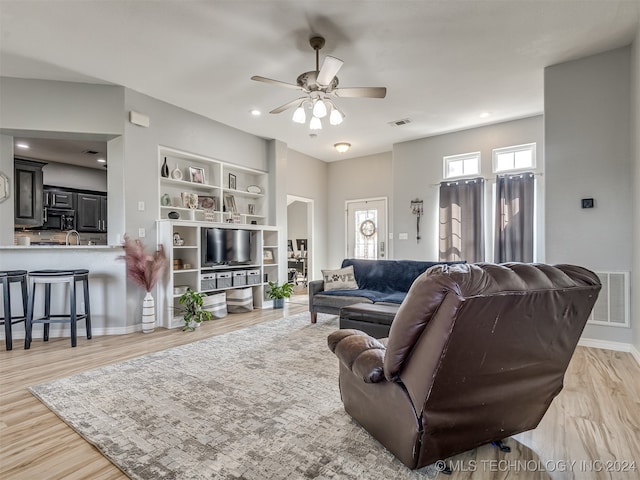 living room featuring ceiling fan, sink, built in features, and light hardwood / wood-style floors