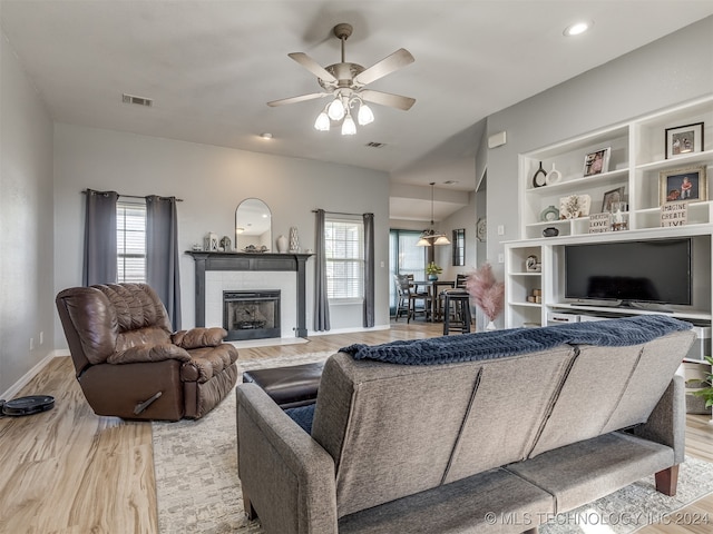 living room featuring ceiling fan, light wood-type flooring, and a tiled fireplace