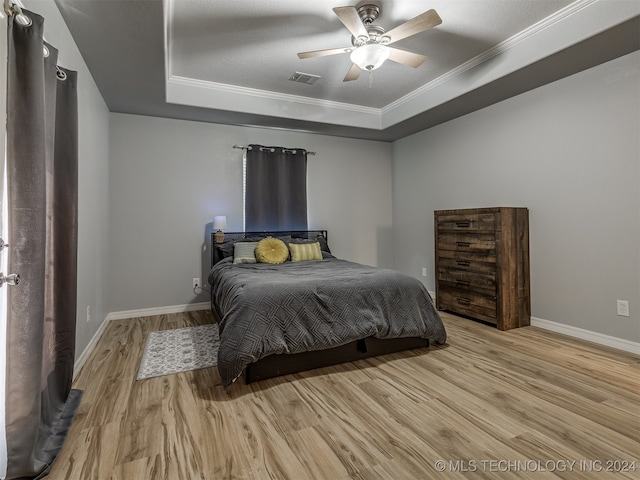 bedroom with light hardwood / wood-style floors, ceiling fan, a tray ceiling, ornamental molding, and a textured ceiling