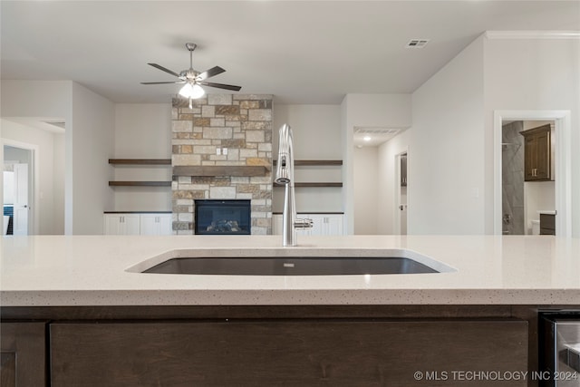 kitchen with ceiling fan, dark brown cabinets, sink, a fireplace, and light stone countertops