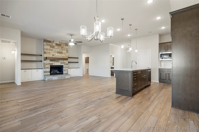 kitchen with light wood-type flooring, dark brown cabinetry, decorative light fixtures, a center island with sink, and a fireplace