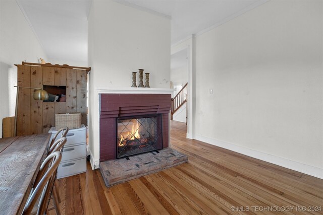 unfurnished living room featuring a brick fireplace, ornamental molding, and hardwood / wood-style floors