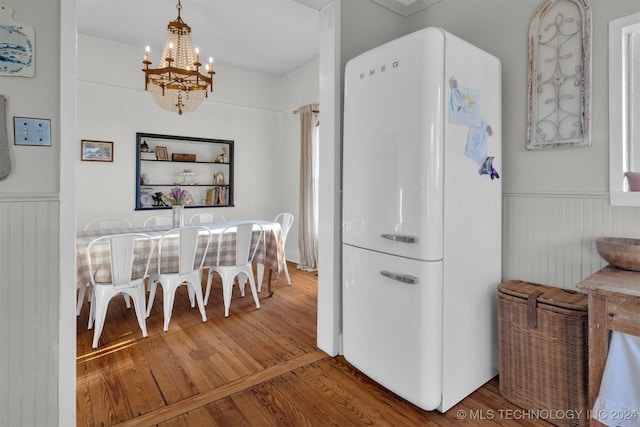 kitchen with white refrigerator, hanging light fixtures, ornamental molding, an inviting chandelier, and hardwood / wood-style floors