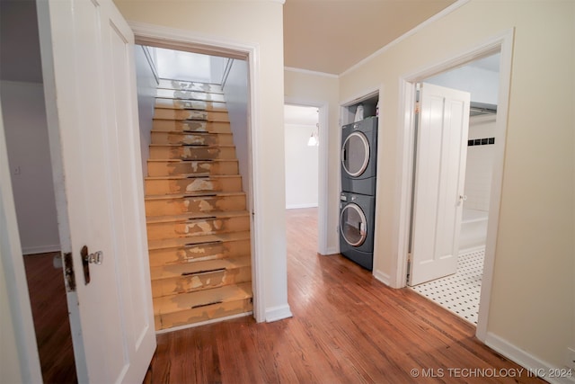 washroom featuring hardwood / wood-style flooring, stacked washer / dryer, and crown molding