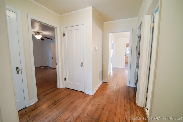 hallway featuring light wood-type flooring, crown molding, and stacked washer / dryer