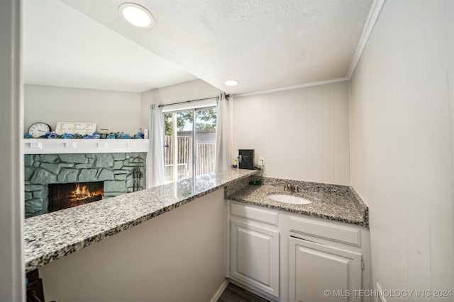 kitchen featuring sink, light stone counters, a stone fireplace, ornamental molding, and white cabinets