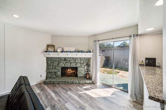 living room featuring wood-type flooring, a textured ceiling, and a stone fireplace