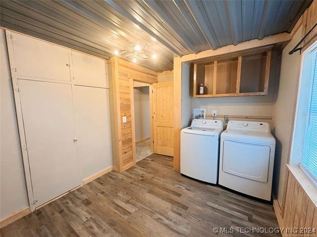 clothes washing area with dark wood-type flooring, independent washer and dryer, wood walls, and cabinets