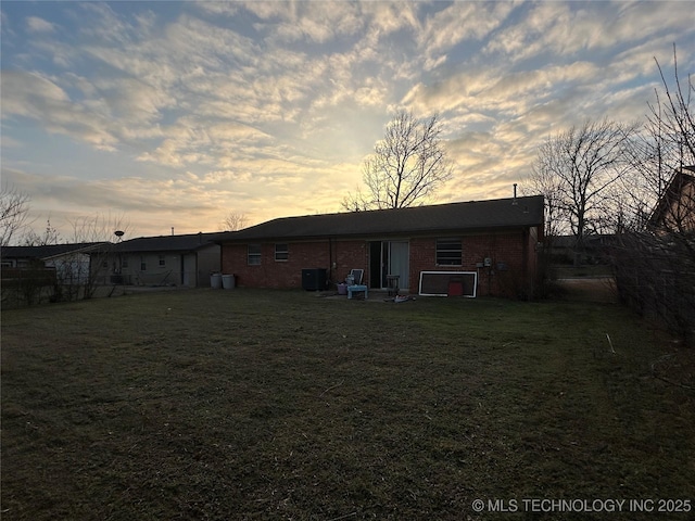 back house at dusk featuring central AC unit and a lawn