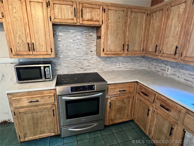 kitchen with appliances with stainless steel finishes, dark tile patterned floors, and decorative backsplash