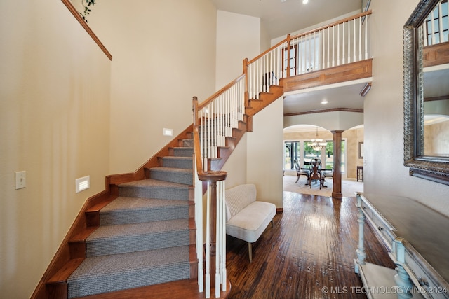 stairway featuring decorative columns, a chandelier, a towering ceiling, and wood-type flooring