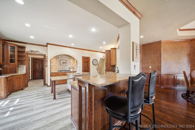 kitchen with light stone counters, a breakfast bar, light hardwood / wood-style floors, kitchen peninsula, and ornamental molding