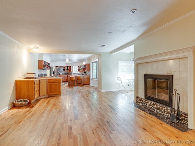 living room with baseboards, ornamental molding, a fireplace, light wood-style flooring, and a textured ceiling