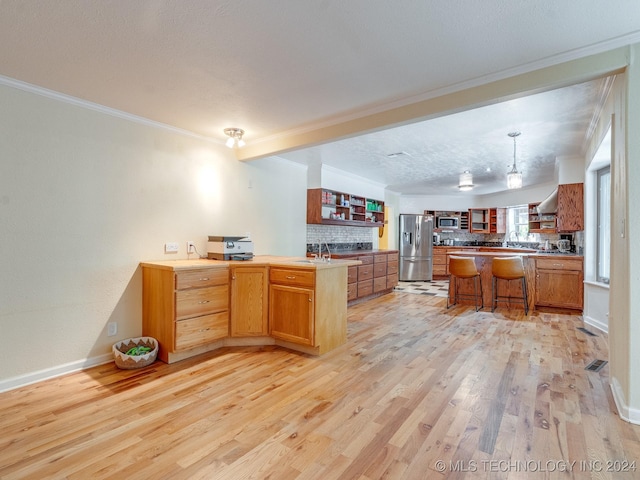 kitchen featuring stainless steel fridge, ornamental molding, light wood-style floors, a kitchen bar, and a peninsula