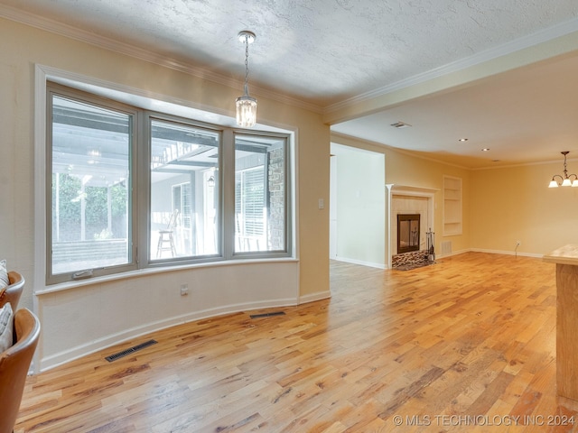 unfurnished living room featuring light wood-style floors, an inviting chandelier, ornamental molding, and visible vents