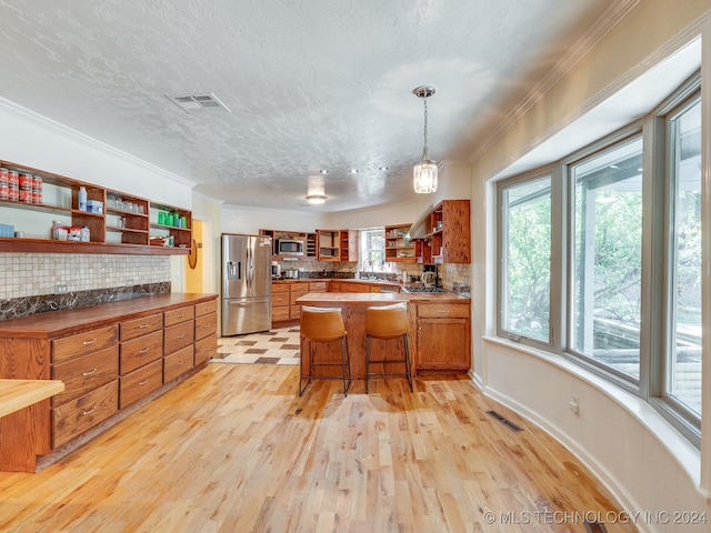 kitchen with light hardwood / wood-style flooring, ornamental molding, backsplash, appliances with stainless steel finishes, and a kitchen bar