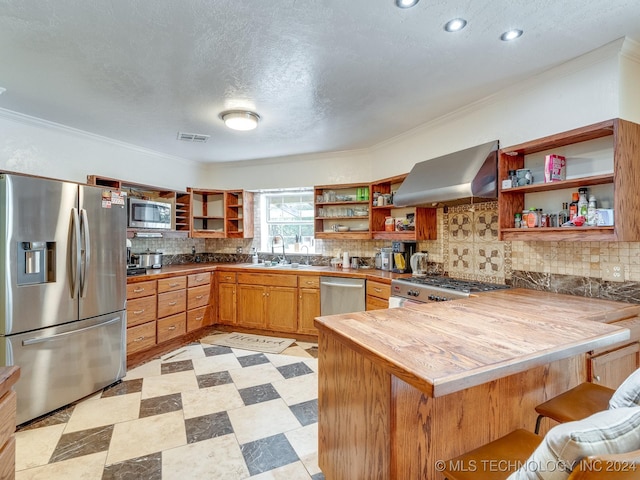 kitchen featuring ornamental molding, a peninsula, open shelves, wall chimney exhaust hood, and appliances with stainless steel finishes