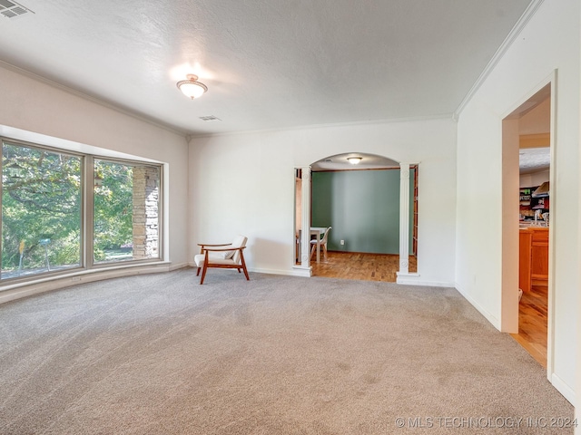 carpeted spare room with arched walkways, visible vents, baseboards, and crown molding