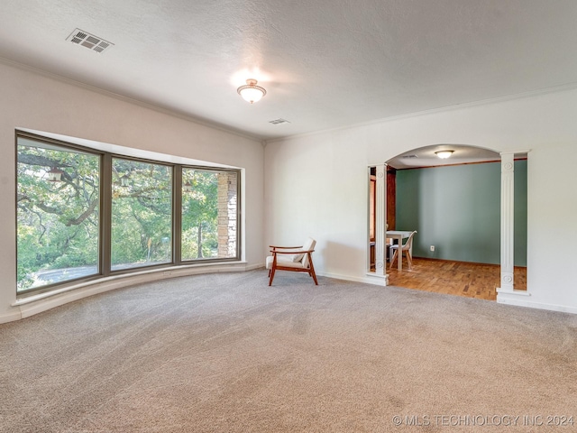carpeted empty room with arched walkways, visible vents, baseboards, and ornamental molding