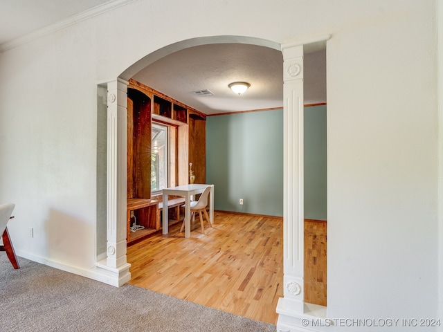 corridor with ornate columns, ornamental molding, wood-type flooring, and a textured ceiling