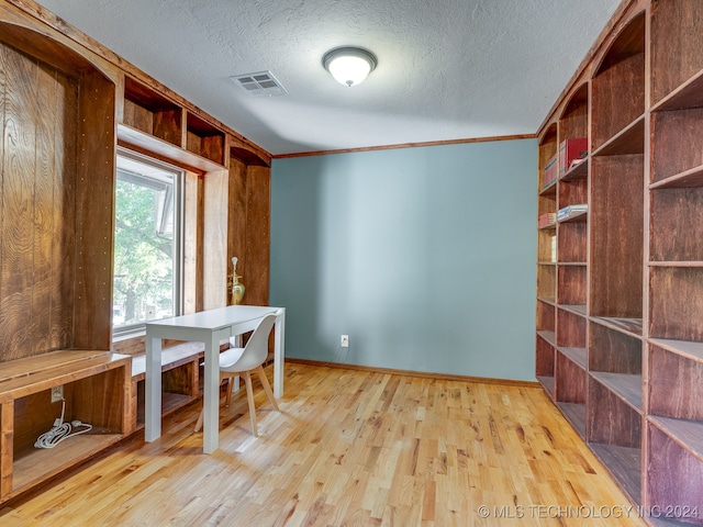 unfurnished dining area featuring a textured ceiling, wooden walls, crown molding, and light hardwood / wood-style floors