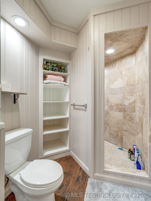 bathroom with a textured ceiling, hardwood / wood-style floors, tiled shower, and toilet